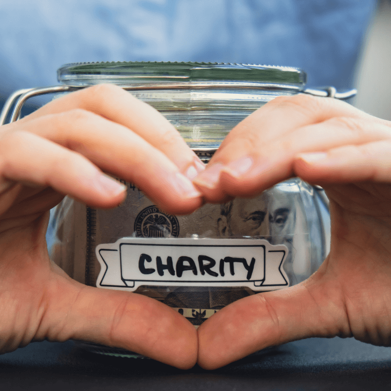 female hand showing heart sign with hands over donation jar