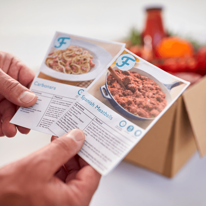 close up of hand in kitchen holding recipe insert cards from box